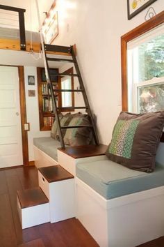 a loft bed sitting under a window next to a wooden floor with stairs leading up to it