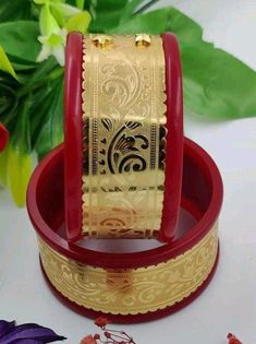 two red and gold jewelry boxes sitting on top of a white table next to flowers