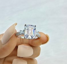 a woman's hand holding a ring with an emerald and diamond center stone on it