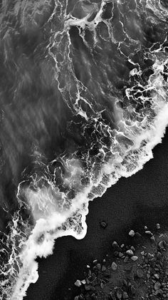 black and white photograph of waves crashing on the beach with rocks in foreground, taken from above