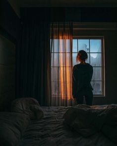 a woman standing in front of a window looking out