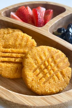 three cookies in a wooden bowl with strawberries and blueberries next to them on a table