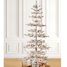 a white christmas tree with presents under it on the floor in front of a wall