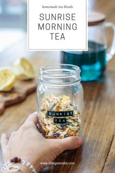 a person holding a jar filled with tea on top of a wooden table