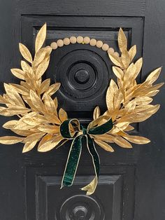 a wreath on the front door of a house with gold leaves and a green ribbon