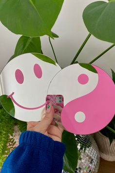 a person holding a cell phone up to a pink and white yin - yang paper mask