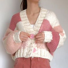 a woman wearing a pink and white cardigan with buttons on the front, standing in front of a wall