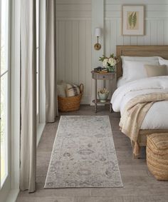 a bedroom with white walls and wood flooring has a large rug on the floor