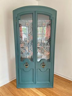 a green corner cabinet with two doors on the front and one door open to reveal another room