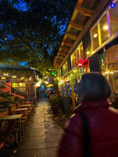 a person standing on a sidewalk in front of a building at night with lights strung from the roof