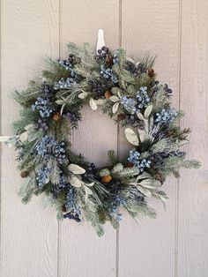 a wreath hanging on the side of a building with pine cones and blue berries around it