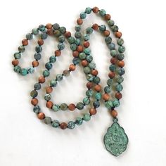 "A Mala for positive change, this Buddha pendant Mala bead necklace from True Nature Jewelry is hand knotted to perfection. It features matte African Turquoise beads that are said to open the mind to new ideas and possibility and help develop positive change in our lives. Sandalwood can be added as a accent bead. A good Mala for working with the Third Eye Chakra, helping to stimulate, and strengthen and clear the center while allowing growth. The unique Buddha pendant dangles with effortless gra Spiritual Beaded Turquoise Necklace For Jewelry Making, Spiritual Turquoise Beaded Necklace With 108 Beads, Handmade Turquoise Beaded Necklaces For Meditation, Spiritual Turquoise Beaded Necklaces With Gemstone Beads, Artisan Turquoise Necklaces With 8mm Beads, Bohemian Beaded Necklaces With 8mm Beads For Jewelry Making, Turquoise Beaded Necklace For Meditation With 8mm Beads, Spiritual Turquoise Gemstone Beaded Necklaces, Artisan Turquoise Necklaces With 108 Beads