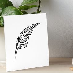 a black and white drawing of a feather on a white card next to a potted plant