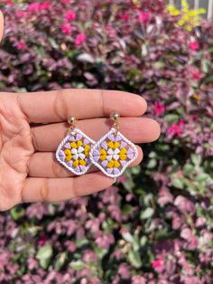 a hand holding a pair of earrings with yellow and pink flowers in the background,