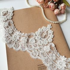 a piece of paper with lace on it next to flowers and pearls in the background