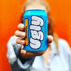 a woman holding up a can of soda in front of her face with an orange background