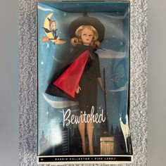 a barbie doll in a box with a red cape and black hat on it's head