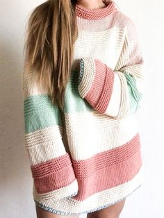 a woman with long hair wearing a striped sweater and hat, standing in front of a white wall