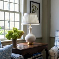 a white lamp sitting on top of a wooden table next to a chair and window