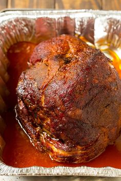 a roasting pan filled with meat and sauce on top of a wooden table next to an orange peel