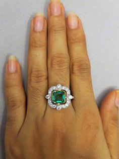 a woman's hand holding an emerald and diamond ring