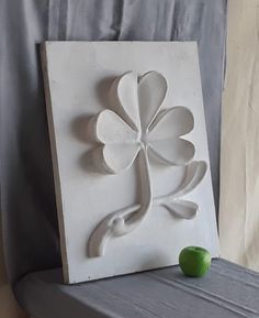 a green apple sitting on top of a table next to a white plaque with a four leaf clover