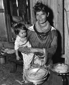 an old black and white photo of a woman holding a child in her arms while cooking