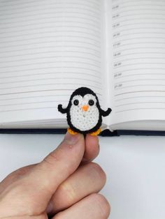 a hand holding a tiny penguin in front of an open book