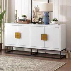 a white cabinet with gold handles in a living room next to a lamp and potted plant