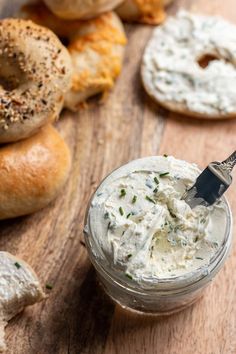 a jar filled with cream cheese sitting on top of a wooden table next to bagels