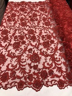 a red lace with flowers on it is laying on a tablecloth that has been folded over