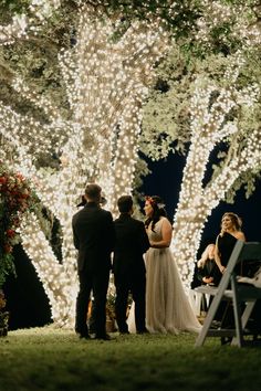 a bride and groom standing under a large tree with white lights on it's branches