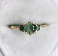 a green ring with three stones in it sitting on a white cloth covered tablecloth