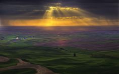 the sun shines brightly through clouds over rolling green hills and fields with trees in the foreground