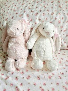 two stuffed animals sitting on top of a bed covered in pink and white floral sheets