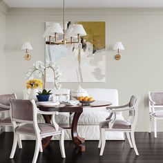 a dining room table with chairs and a white couch in front of a painting on the wall