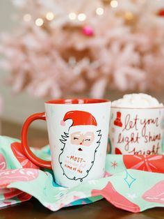 two coffee mugs with santa's face on them sitting next to a christmas tree