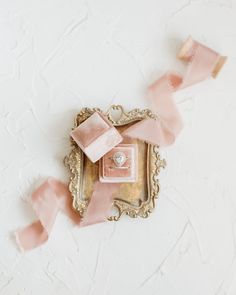 pink ribbon tied around an ornate frame with a ring in it on the wall next to another piece of art