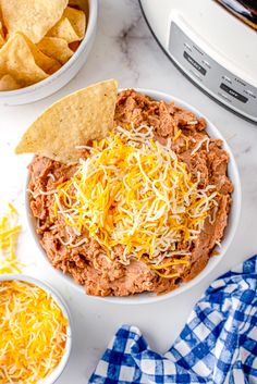 a white bowl filled with chili cheese and tortilla chips next to a crock pot