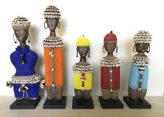 five african style figurines are lined up on black bases and stand against a white wall