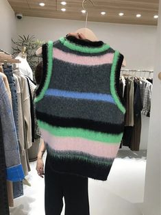 a woman standing in front of a rack of clothes wearing a sweater with multicolored stripes