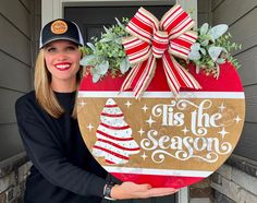 a woman holding up a wooden sign that says tis the season