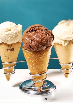 three scoops of ice cream sitting on top of a metal stand in front of a blue wall