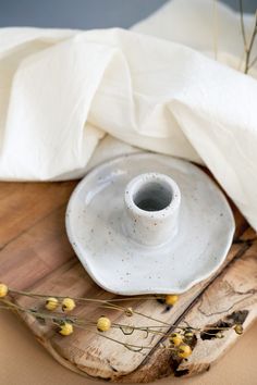 a white cup and saucer sitting on top of a wooden cutting board next to flowers