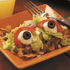 an orange plate topped with lettuce covered in googly eyes and tomato slices