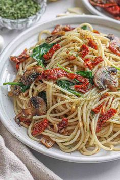 mushroom and spinach spaghetti with sun - dried tomatoes on a white plate next to silverware