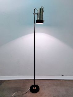 a lamp that is on top of a floor in a room with a wall behind it