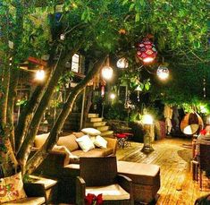 an outdoor seating area is lit up at night with lights on the trees and hanging decorations