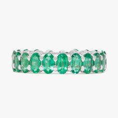 an emerald colored ring is shown on a white background and has five oval cut stones in the middle