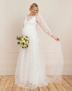 a pregnant woman in a white wedding dress holding a bouquet and posing for the camera